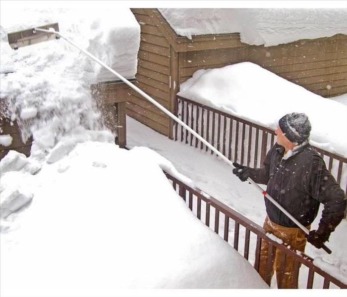 Man removing snow from roof with a rake
